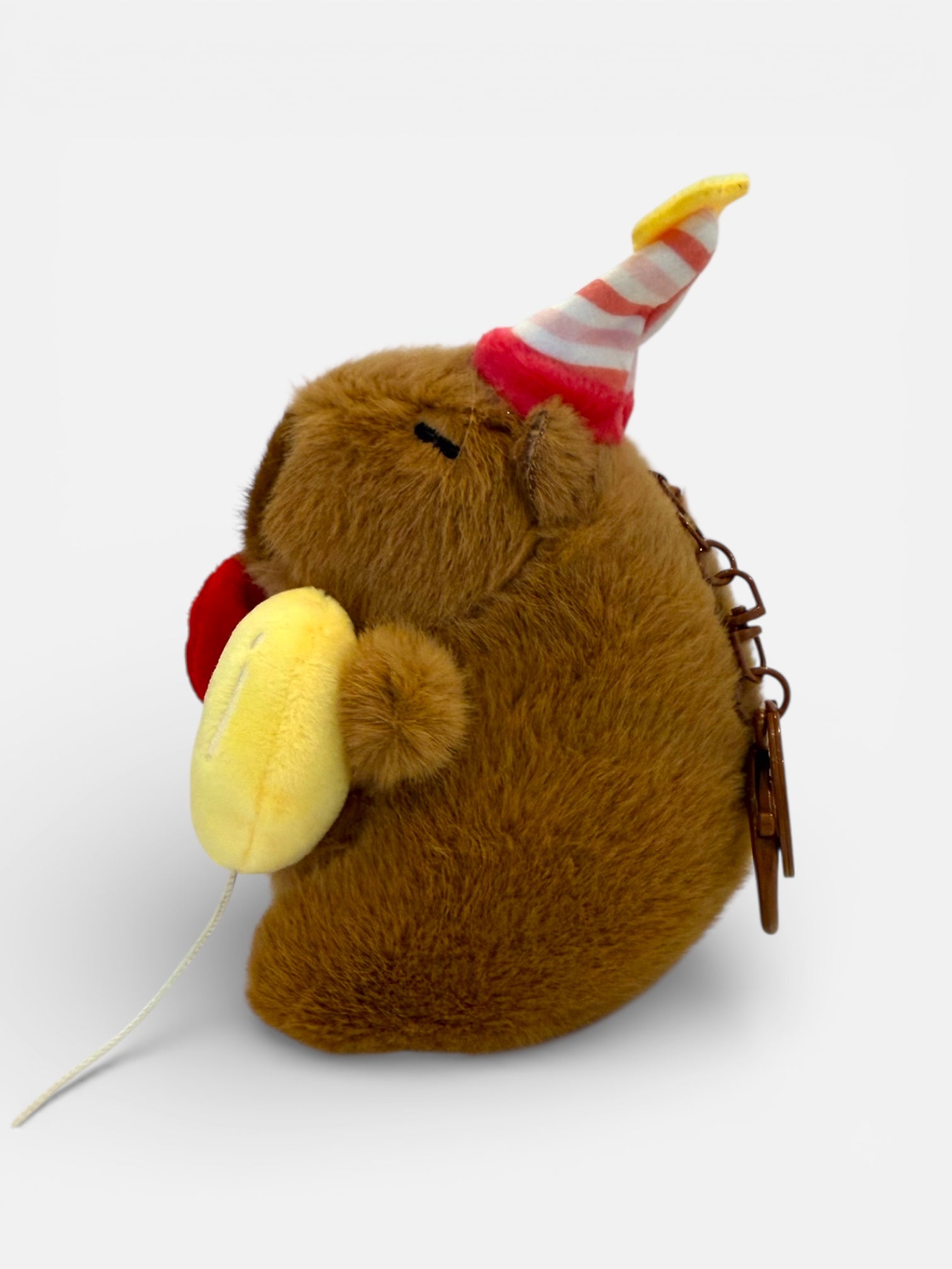 Plush toy resembling a Capybara with a party hat and balloon, on a white background