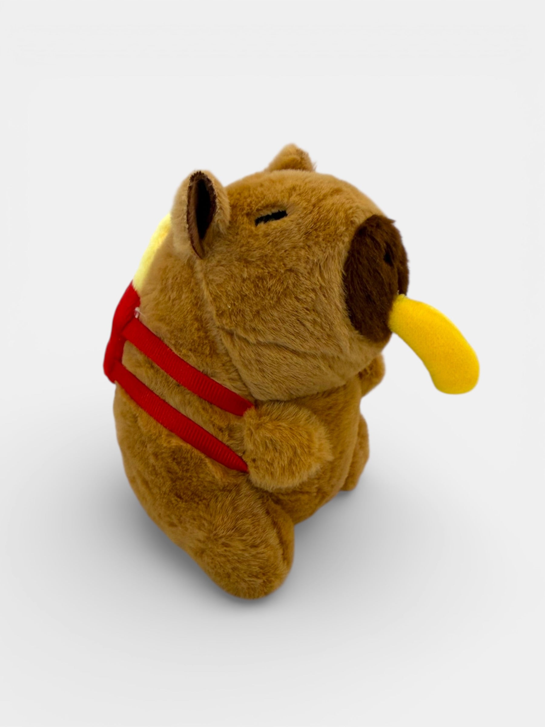 Brown plush Capybara with a red backpack and yellow object on a white background