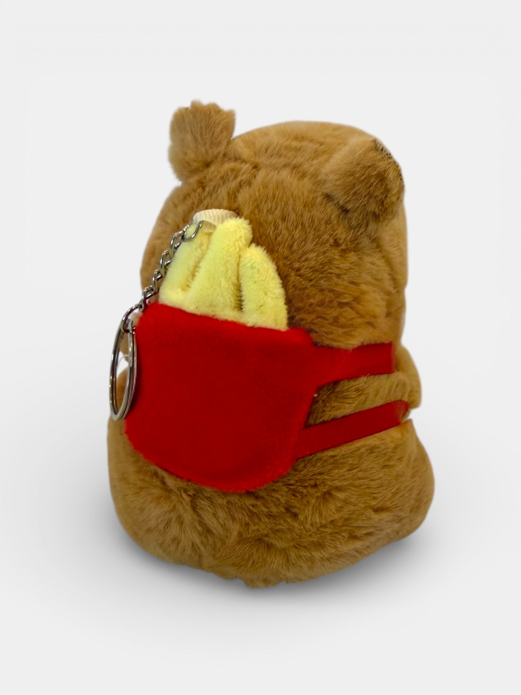 Plush Capybara keychain with a red pocket and yellow item inside on a white background