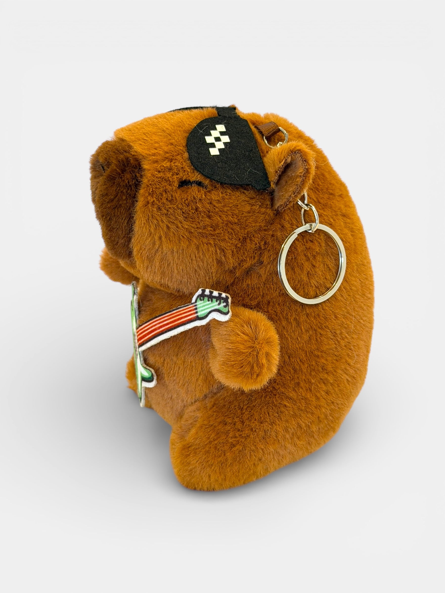Plush Capybara toy with a guitar and ring on a light gray background