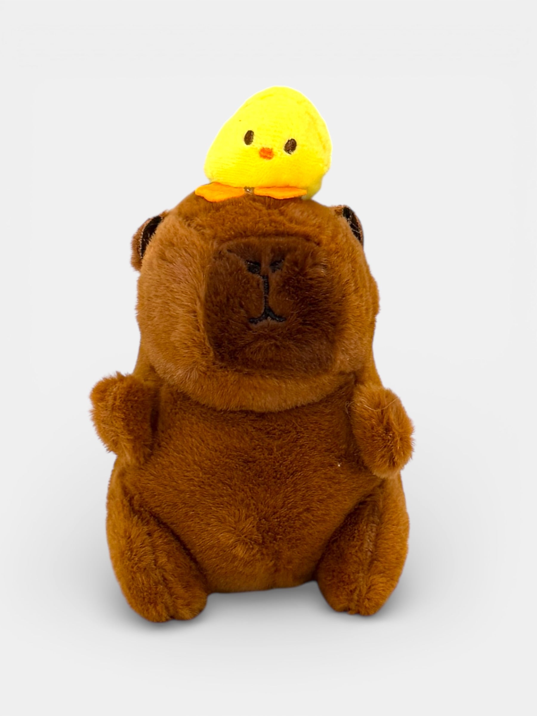 Plush toy Capybara with a yellow chick on its head against a white background