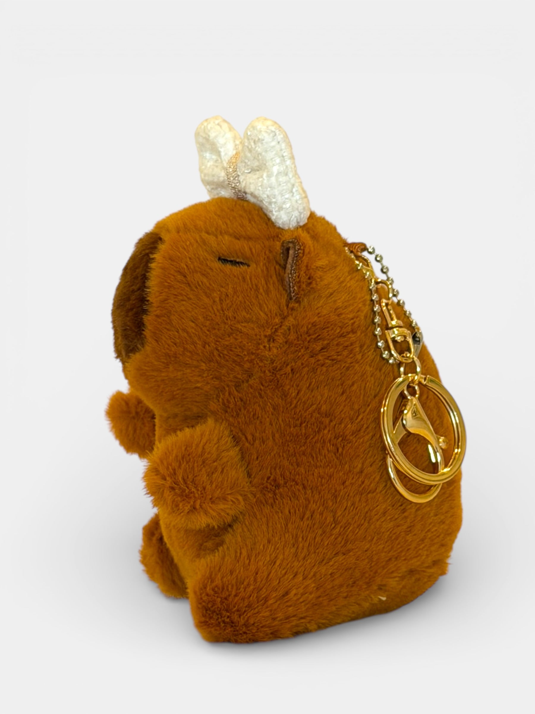 Brown plush Capybara keychain with gold chain and bird charm on a white background